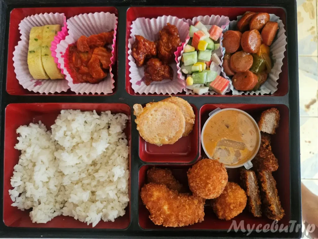 MyCebuTrip Korean lunch box featuring assorted fried dishes, sausage stir-fry, and rolled omelet served during the island hopping tour.