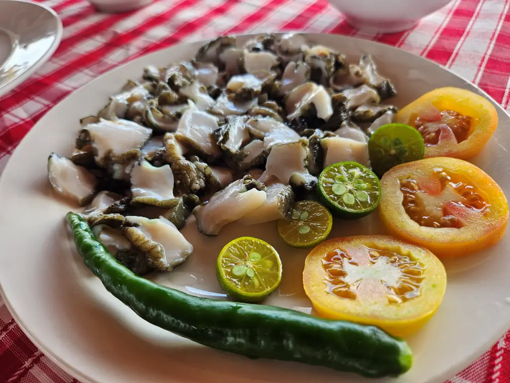 Fresh raw conch sashimi slices served with calamansi and tomatoes