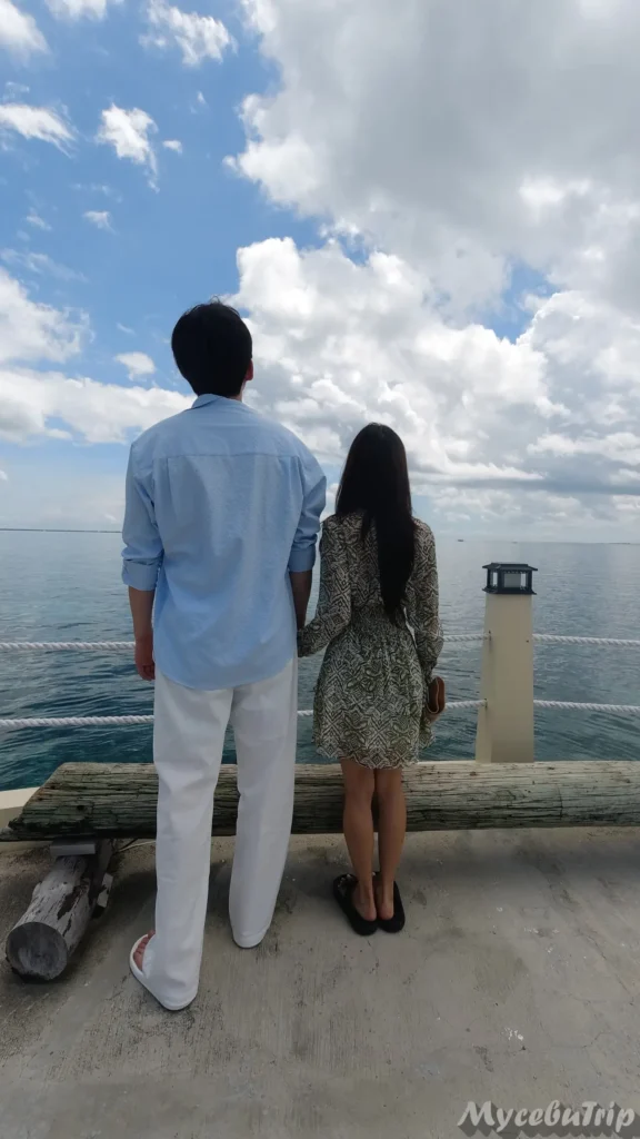 Couple standing on the wooden bridge at Nalusuan Island looking at the sea
