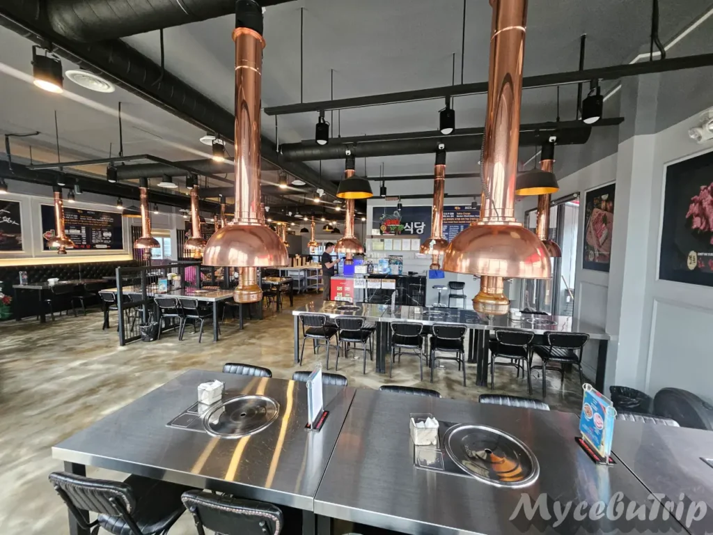 Interior of the spacious dining hall with stainless steel tables and copper-colored exhaust hoods hanging over the grills.