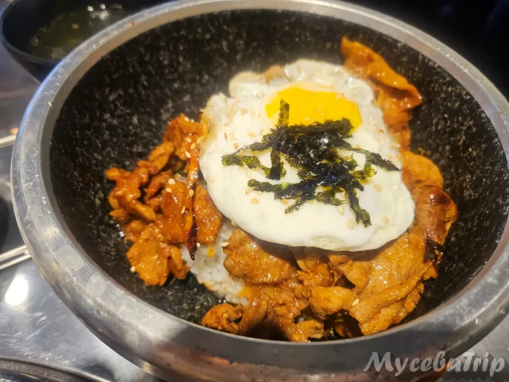 A bowl of Jeyuk Deopbap (Spicy Pork Over Rice) topped with a fried egg and shredded seaweed.