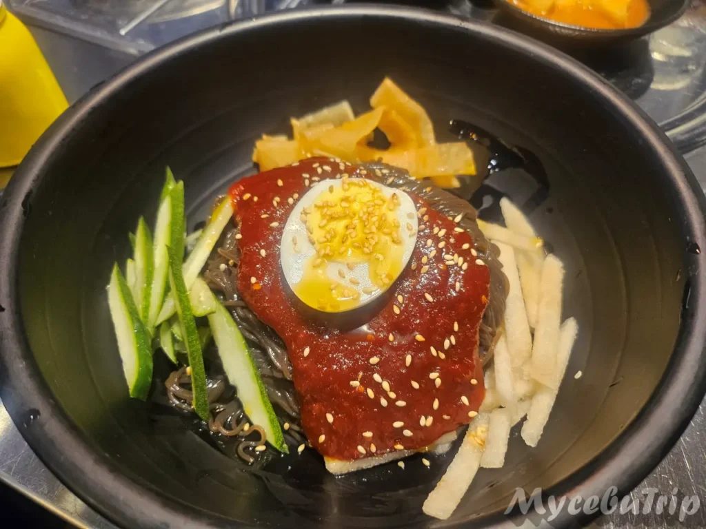 A serving of Bibim Naengmyeon (Spicy Cold Noodles) garnished with a hard-boiled egg, cucumber, and spicy sauce.
