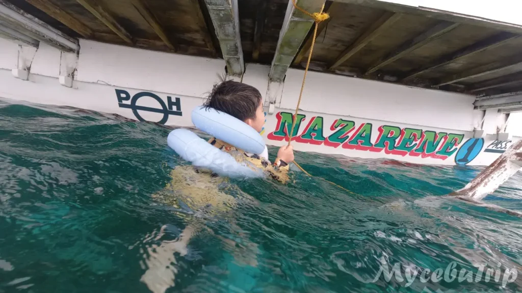 A child taking a break holding onto a rope next to the Bangka boat hull.